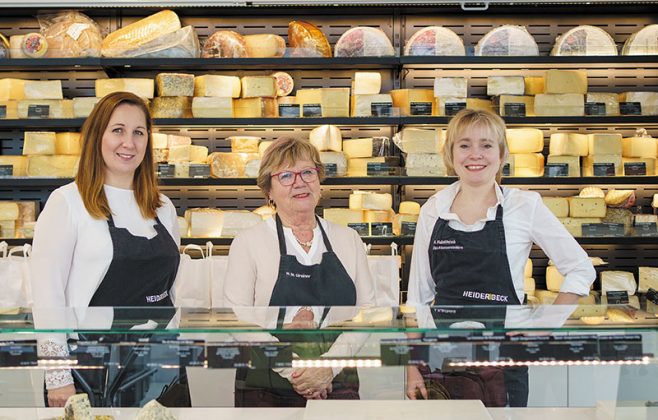 Mercedes Nemeth, Rosa Greiner und Anna Majdic stehen an der Theke im Heiderbeck Feinkost Outlet, im Hintergrund das Käseregal