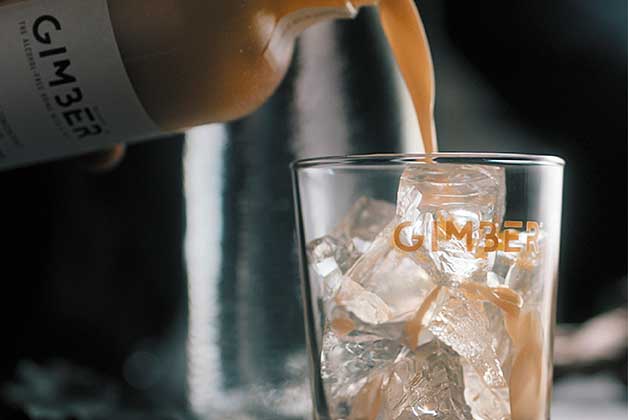 Ein Glas mit Eiswürfeln wird mit dem Gimber Ingwerdrink befüllt
