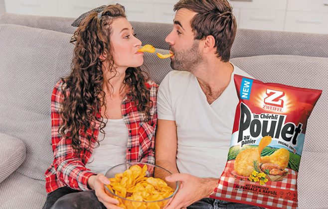 Ein Paar sitzt auf dem Sofa und hat eine Schüssel Chips in der Hand. Beide haben einen Chip im Mund und schauen sich an