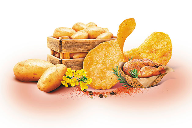 Eine Holzkiste mit Kartoffeln, davor einige Chips und ein Brathähnchen in einem Korb
